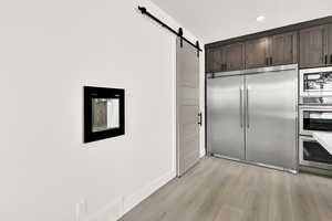 Kitchen with built in appliances, a barn door, dark brown cabinets, light countertops, and light wood-type flooring