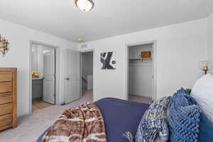 Bedroom featuring a closet, light colored carpet, visible vents, and ensuite bathroom