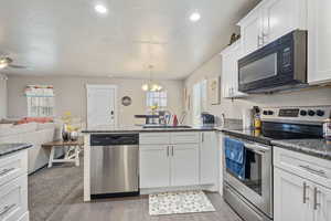 Kitchen featuring stainless steel appliances, a sink, white cabinetry, and decorative light fixtures