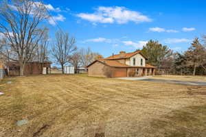 View of property exterior featuring a chimney, a lawn, a storage shed, an attached garage, and fence