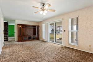 Unfurnished living room featuring wallpapered walls, baseboards, ceiling fan, stairway, and carpet floors