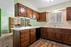 Kitchen with a peninsula, wood finished floors, a sink, light countertops, and dishwasher