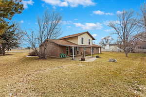 Back of property featuring brick siding, a lawn, an outdoor fire pit, a patio area, and fence