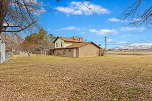 View of side of home with a yard, brick siding, a mountain view, and a chimney