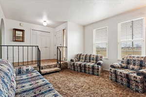 Carpeted living room featuring a textured ceiling, arched walkways, and baseboards