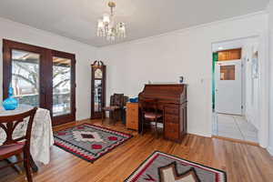 Home office with ornamental molding, light hardwood / wood-style floors, an inviting chandelier, and french doors