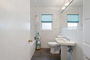 Bathroom with wood-type flooring, tile walls, toilet, and shower / bath combination with curtain