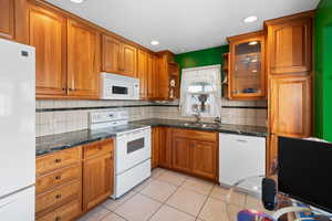 Kitchen with light tile patterned flooring, sink, white appliances, and decorative backsplash