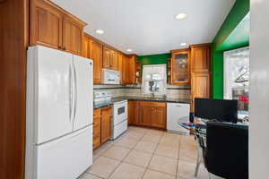 Kitchen featuring white appliances, light tile patterned floors, sink, and decorative backsplash