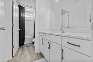 Bathroom featuring toilet, wood finished floors, visible vents, vanity, and shower / bathtub combination with curtain