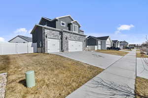 View of side of home with concrete driveway, a lawn, fence, a residential view, and stone siding