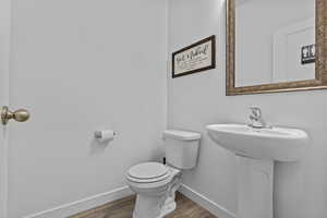 Half bathroom featuring toilet, baseboards, and wood finished floors