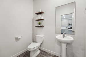 Half bathroom with toilet, baseboards, and wood finished floors