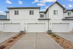View of front of house with driveway, an attached garage, board and batten siding, and central AC