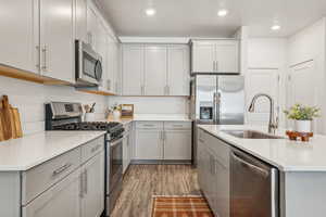 Kitchen featuring light countertops, stainless steel appliances, a sink, light wood-style floors, and gray cabinets