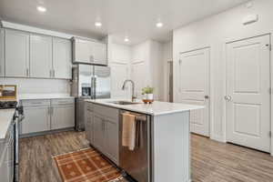 Kitchen with light countertops, gray cabinets, a sink, appliances with stainless steel finishes, and wood finished floors