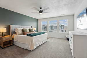 Bedroom featuring a textured ceiling, visible vents, baseboards, ceiling fan, and light carpet