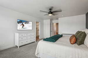 Carpeted bedroom featuring a ceiling fan, ensuite bath, baseboards, and a textured ceiling
