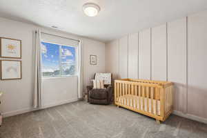 Carpeted bedroom featuring a crib, a textured ceiling, baseboards, and visible vents