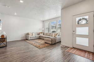 Living area featuring baseboards, a textured ceiling, wood finished floors, and recessed lighting
