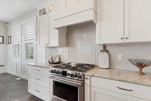 Kitchen featuring glass insert cabinets, light stone counters, high end stainless steel range oven, custom exhaust hood, and white cabinetry