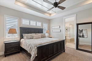 Bedroom featuring baseboards, ensuite bathroom, a raised ceiling, and light colored carpet