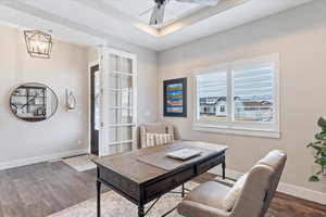 Office space with ceiling fan with notable chandelier, a raised ceiling, wood finished floors, and baseboards