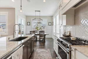 Kitchen with light stone counters, decorative light fixtures, stainless steel appliances, dark wood-type flooring, and a sink