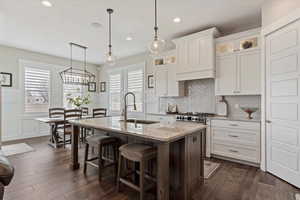 Kitchen featuring stainless steel range, glass insert cabinets, white cabinets, a sink, and a kitchen island with sink