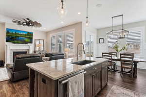 Kitchen featuring light stone countertops, dark brown cabinetry, a sink, and decorative light fixtures