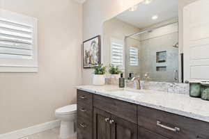 Bathroom with toilet, vanity, baseboards, tile patterned floors, and a stall shower