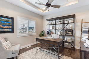 Home office with ceiling fan, a tray ceiling, baseboards, and wood finished floors