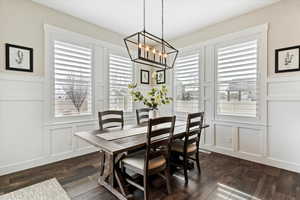 Dining area with dark wood-style floors, a chandelier, and a decorative wall