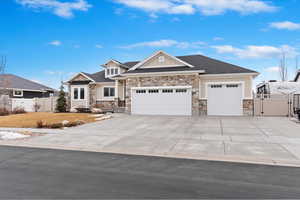 View of front of home with an attached garage, fence, stone siding, driveway, and a gate