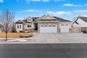 View of front facade featuring a garage, stone siding, concrete driveway, and a gate