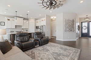 Living room featuring dark wood-style floors, ceiling fan with notable chandelier, baseboards, and recessed lighting