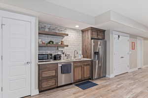 Bar with appliances with stainless steel finishes, light wood-type flooring, a sink, and decorative backsplash