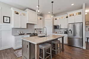 Kitchen with premium appliances, glass insert cabinets, a sink, white cabinets, and a center island with sink