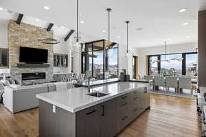 Kitchen with open floor plan, hanging light fixtures, a kitchen island with sink, light countertops, and dark brown cabinets