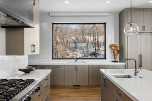 Kitchen with island exhaust hood, light countertops, hanging light fixtures, a sink, and modern cabinets