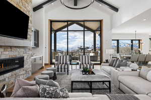 Living room with high vaulted ceiling, beamed ceiling, wood finished floors, and a stone fireplace