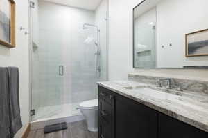 Full bath featuring toilet, a stall shower, wood finished floors, and vanity