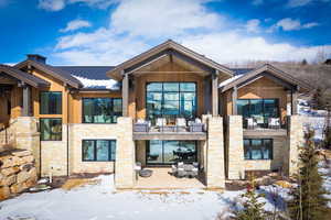 Snow covered back of property featuring stone siding, a standing seam roof, metal roof, and a balcony