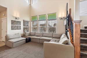 Living area featuring carpet, stairway, and a high ceiling