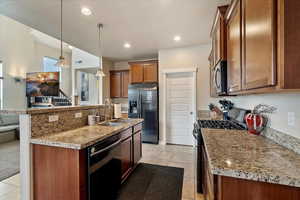 Kitchen with a kitchen island with sink, a sink, black appliances, brown cabinetry, and decorative light fixtures