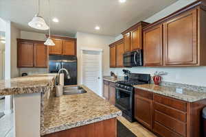 Kitchen with light countertops, a sink, black gas range, and a center island with sink