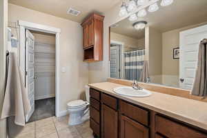 Bathroom with toilet, vanity, visible vents, tile patterned floors, and a walk in closet