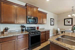 Kitchen featuring light tile patterned floors, a sink, stainless steel microwave, range with gas cooktop, and an inviting chandelier