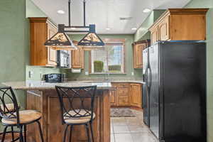 Kitchen featuring light tile patterned floors, black appliances, a sink, and a kitchen breakfast bar