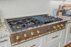 Details featuring white cabinetry, stainless steel gas stovetop, decorative backsplash, and light stone countertops